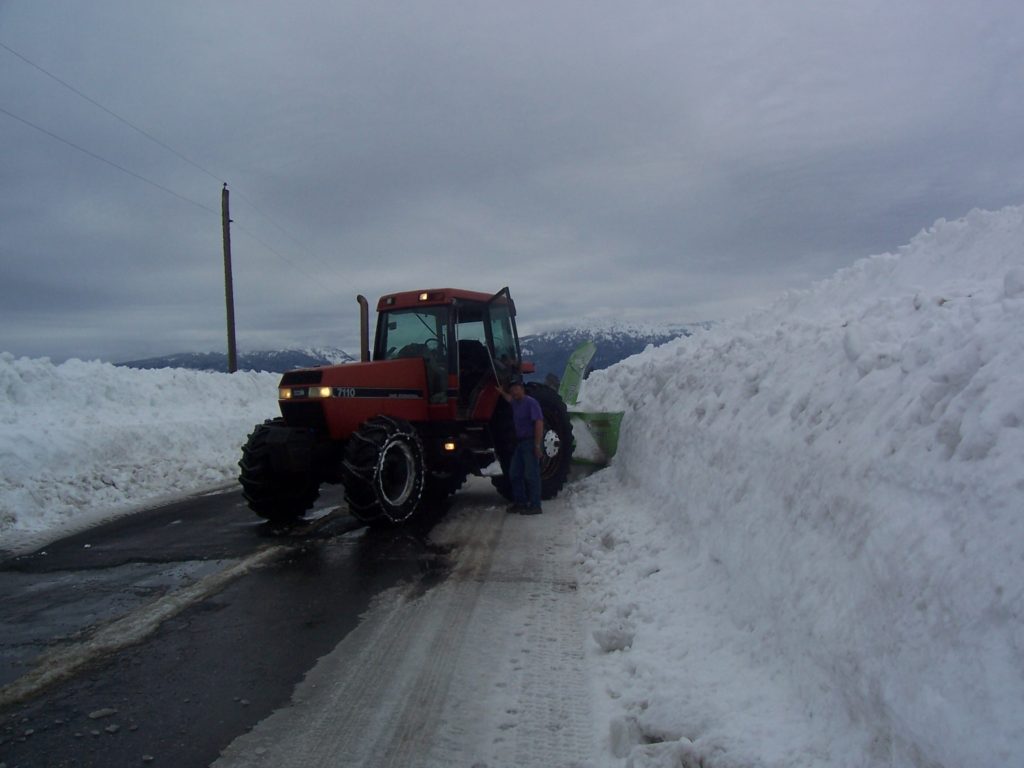 My Farmer standing beside his tractor parked in the county road next to the snow bank.